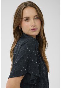 Blusa nera con pois bianchi, maniche corte con volant, tessuto morbido e vestibilità comoda. Design minimalista con dettagli delicati.