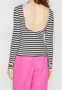 Randig långärmad topp i svart och vitt med djup scooped bak. Matchad med högmidjade rosa byxor som visar en figurnära och kort design.