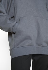 Sweatshirt gris avec une coupe décontractée, des poignets et un ourlet côtelés, et une poche kangourou. La texture du tissu semble douce avec une finition mate.