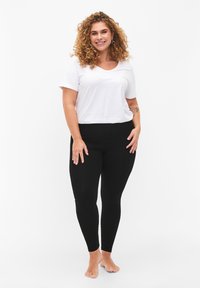 Black leggings paired with a white short-sleeve t-shirt. T-shirt has a scoop neckline; leggings are form-fitting with a smooth texture.