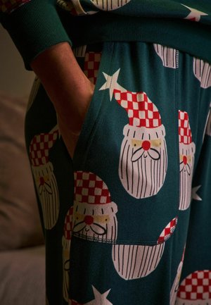 Zelené pyžamové kalhoty se vzorem sezónního Santa Claus obličeje, s červenými kostkovanými čepicemi a bílými vousy, vyrobené z měkkého materiálu.