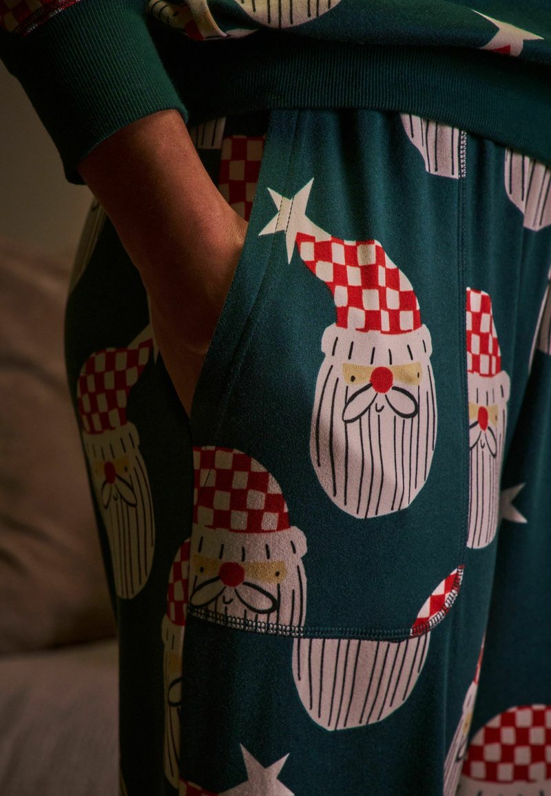 Gröna pyjamasbyxor med ett säsongsmönster av jultomtar, med rödrutiga hattar och vita skägg, i en mjuk tygtextur.
