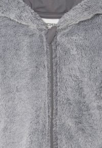 Haut en molleton zippé gris avec une texture douce et pelucheuse et une capuche doublée. Il présente une fermeture éclair centrale et un minimum de détails.