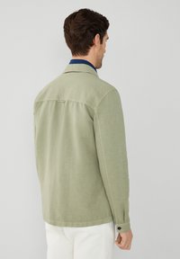 Giacca camicia verde chiaro con una vestibilità rilassata, dotata di colletto, polsini abbottonati e dettaglio sul retro. Tessuto con texture.