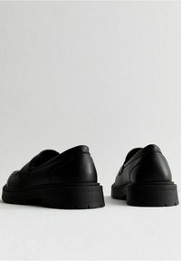 Scarpe in pelle nera con forma arrotondata e suola voluminosa. Presentano dettagli di cucitura sottili e design slip-on, adatte per un look informale.