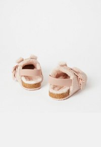 Vaaleanpunaiset taaperon sandaalit, joissa on tekoturkista valmistettu vuori, teksturoitu kangas päällinen, säädettävät hihnat ja korkkityyppiset pohjat. Kevyet nauhaakennukset takana.