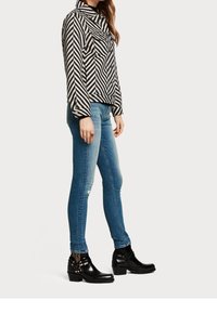 Mustat ja valkoiset raidalliset pitkähihaiset paita, jossa on kaulus, yhdistettynä sinisiin kapeisiin farkkuihin ja mustiin nilkkureihin, joissa on koristeluun käytetty metallisosia.