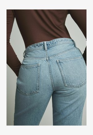 Jeans din denim bleu deschis cu talie înaltă, buzunare pe spate și o ușoară decolorare. Textura este netedă, cu cusături și ușoare deteriorări.