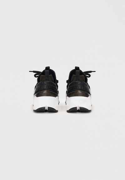 Zapatillas deportivas negras con tejido texturizado y acentos sintéticos, que cuentan con una suela blanca gruesa y un detalle en el talón texturizado en negro.