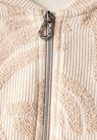 Chaqueta cremosa de cremallera con tejido texturizado con rayas verticales y un diseño estampado; herrajes de cremallera en plata con un tirador distintivo.