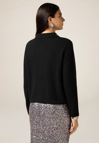 Maglione nero e testurizzato con scollo a collo, abbinato a una gonna argento scintillante con paillettes. Presenta un'orlo aderente e maniche larghe.