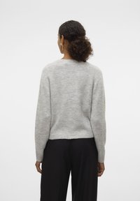Gray knit sweater with a soft texture, crew neckline, and raglan sleeves. The fit is relaxed, ending just above the waistband of black pants.