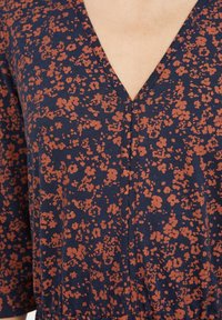 Robe en tissu marine avec un motif floral couleur rouille, décolleté en V et manches courtes avec une taille froncée pour un style décontracté.