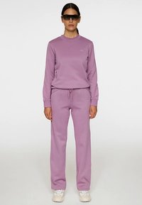 Paarse sweatshirt met ronde hals en bijpassende paarse joggingbroek, gemaakt van zachte stof. Voorzien van een logo op de borst en een taille met trekkoord.