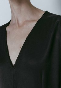 Sort v-udskæringstøj med en blød, glat tekstur og en rå kantfinish. Den lave udskæring fremhæver décolletéområdet.