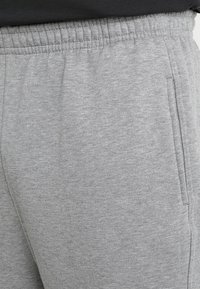 Pantalones de chándal grises hechos de un tejido suave, con cinturilla elástica y bolsillos laterales, que presentan una textura lisa y un corte relajado.