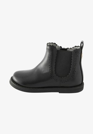 Stivale alla caviglia in pelle nera con bordi scallop, pannelli laterali elastici e perforazioni decorative. Texture liscia e design della punta arrotondata.