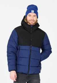 Blå och svart puffjacka med huva, med quiltade sektioner, dragkedjestängning och två sidofickor. Stickad blå mössa som tillbehör.