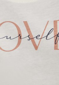 Weißer Stoff mit weicher Textur, auf dem der Text "LIEBE dich selbst" in Pfirsich und Dunkelblau zu sehen ist, mit unterschiedlichen Schriftarten und -größen.