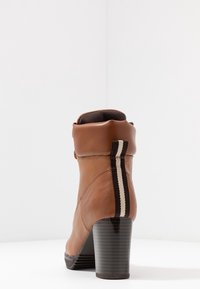 Bottine en cuir marron avec un talon effilé, dotée d'un accent élastique rayé à l'arrière et d'une texture lisse.