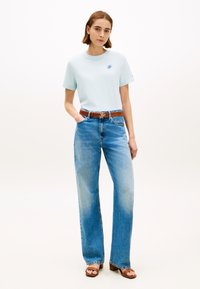 T-shirt en coton bleu clair avec un col rond, associé à un jean bleu délavé taille haute avec jambes larges. Ceinture marron avec une boucle en métal. Sandales à talons marron.