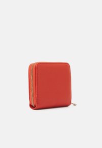 Portefeuille carré en cuir rouge texturé, avec une fermeture éclair dorée courant le long du bord supérieur et une petite languette de tirage sur le côté.