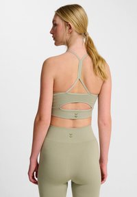 Olivgrön sport-bh med design av korsade band, har en öppen rygg och dubbellagerskonstruktion. Texturerad tyg med subtil varumärkeslogotyp.