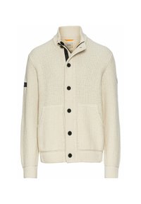 Strik cardigan i creme med sorte knapper, med en stående krave, påsyede lommer og ribbede cuffs og kant. Teksturert mønster hele vejen igennem.