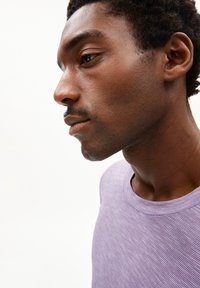 Lichtpaarse gestreepte t-shirt met een ronde halslijn. Toont een close-up profiel van een persoon met een textuur huid en donker krullend haar.