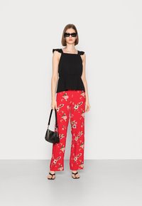 Top peplum preto com alças franzidas, combinado com calças largas vermelhas com flores. Uma bolsa preta e sandálias pretas completam o look.