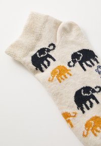 Calcetines beige con patrones de elefantes negros y naranjas, tejido texturizado, con un puño acanalado y un tejido suave para mayor comodidad.