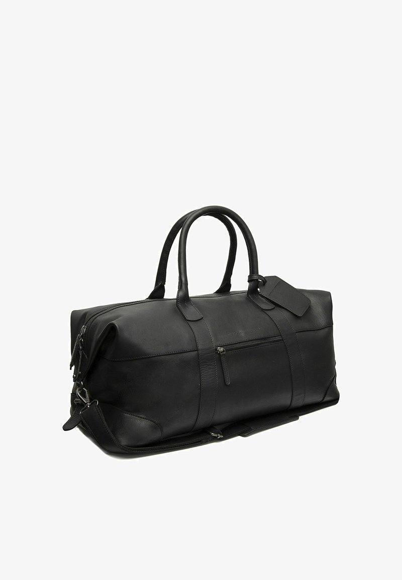 Sac de voyage en cuir noir avec poignées doubles, poche zippée à l'avant, bandoulière amovible et étiquette de bagage attachée, présenté sur un fond blanc.