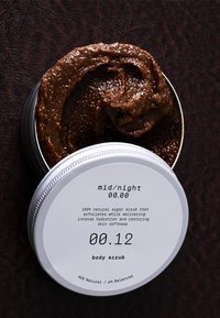 Brunt sockerskrubb i en silverfärgad metallburk. Locket har en vit etikett med svart text; skrubben har en tjock, strukturerad konsistens.