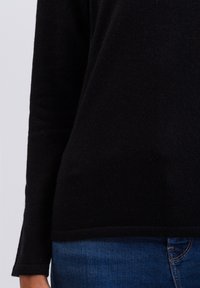 Czarny sweter z długim rękawem wykonany z miękkiego materiału, z prostym wykończeniem, zestawiony z niebieskimi dżinsami. Prosty krój bez widocznych ozdób.