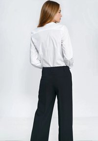 Biała koszula z długim rękawem i kołnierzykiem w połączeniu z dopasowanymi czarnymi spodniami, charakteryzującymi się eleganckim krojem i dwoma tylnymi kieszeniami.