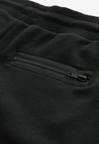 Shorts de sport noirs à texture lisse, avec une poche zippée de couleur sombre assortie et une ceinture côtelée.