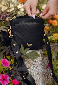 Černá kožená crossbody taška s texturovaným povrchem, zlatými kovovými doplňky a prošívaným vzorem. Obsahuje nastavitelný popruh a detail loga.