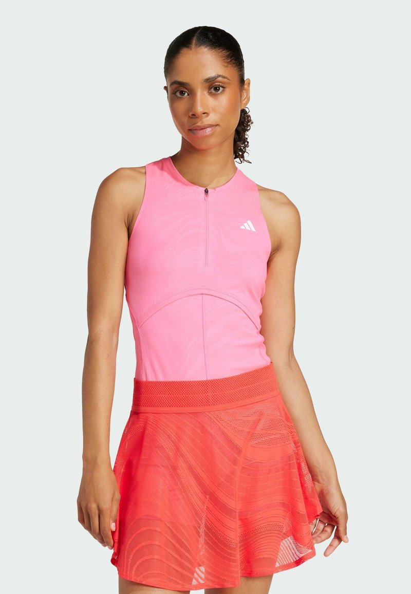 Särskilt rosa sporttopp med framdraget blixtlås, kombinerad med en utsvängd röd nätkjol som har ett vågigt mönster och en texturerad midjeresår.