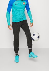 Nike sportskläder som består av en teal långärmad topp med svarta detaljer och svarta tapered byxor, tillsammans med ljusblå fotbollsskor och en fotboll.