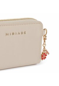 Beige faux leren portemonnee met gouden rits en MIRIADA-logo. Voorzien van een decoratieve charm met een rode bloem en een klein label.