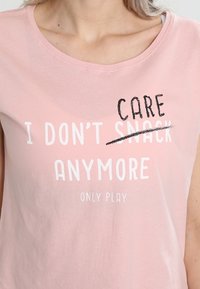 Žena v růžovém tričku s nápisem „Už nepožučuji“ s přeškrtnutým slovem „požučuji“ nahrazeným slovem „pečuji“ a pod tím „jen hraji“.
