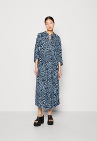 Robe maxi en motif zèbre bleu et noir, faite d'un tissu léger, avec un col rond et une fermeture à nouer, ainsi que des manches 3/4.