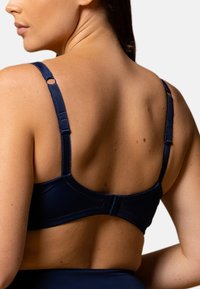 Soutien-gorge bleu foncé avec des bretelles ajustables et un design épuré, doté d'une fermeture à crochet et de détails de couture minimaux au dos.