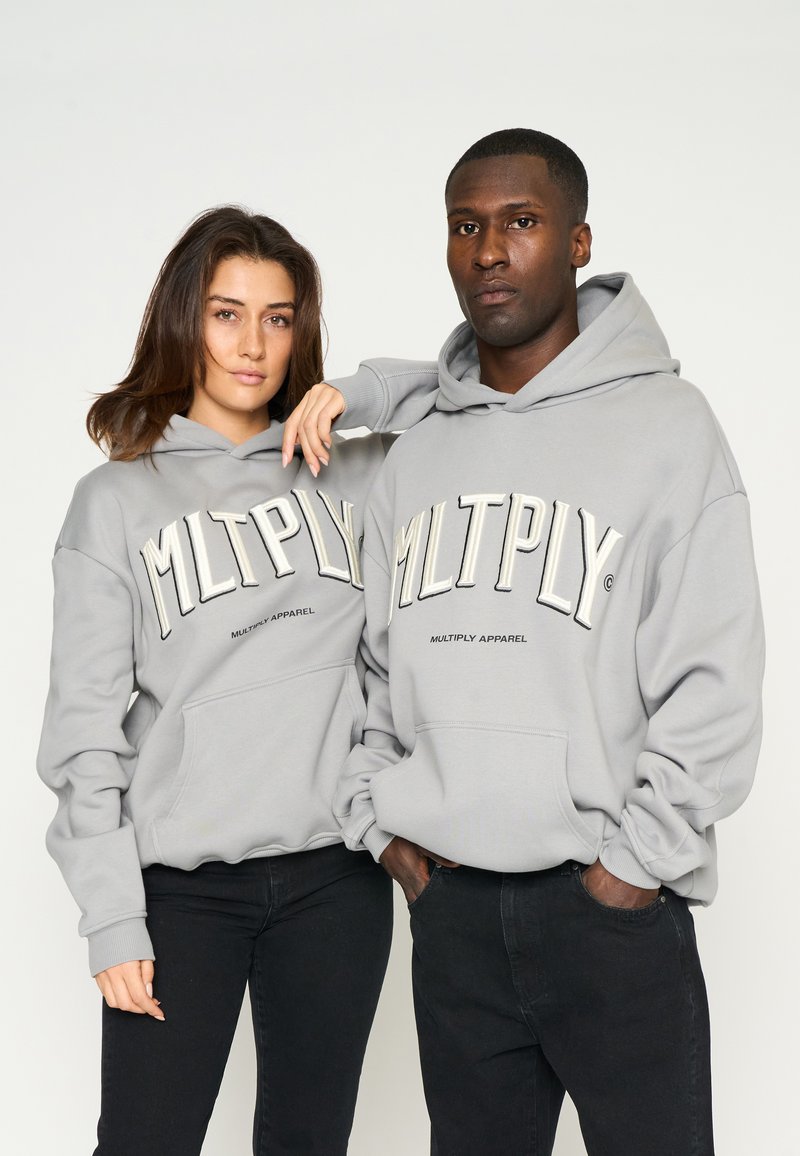 Grijze hoodies met grote "MLTPLY" tekst en "MULTIPLY APPAREL" logo. Katoenmix materiaal, oversized pasvorm, voorkruiszakken en ribgebreide manchetten.