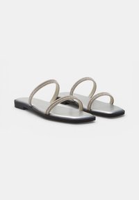 Sandalias planas plateadas con punteras cuadradas, con dos finas tiras adornadas con pedrería a lo ancho del pie y una suela negra.