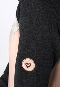 Camisa de manga larga gris oscuro con un panel en gris claro y rosa pastel. Cuenta con un parche circular con un coraz�ón y el texto: "Estamos vivos y activos."