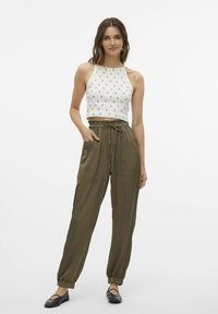 Débardeur blanc court avec imprimé floral rouge ; pantalon vert olive avec cordon de serrage et deux poches devant ; chaussures plates noires ; fond blanc uni.