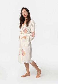 Biela textúrovaná robá s koralovými vzormi v oranžovej a ružovej farbe; má opasok v páse a strapce pozdĺž lemovania.