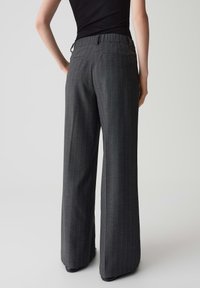 Pantalons gris à rayures avec une coupe ample, taille élastique et poches latérales, représentés de l'arrière. Texture de tissu lisse.