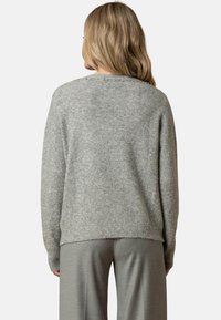 Maglione grigio lavorato a maglia con una vestibilità rilassata, caratterizzato da una finitura testurizzata e un collo decorato. Abbinato a pantaloni grigi a gamba larga.